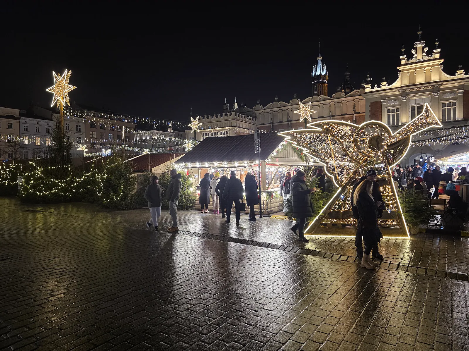 Lit market stalls, a light-up angel and stars in front of the Cloth Hall at night